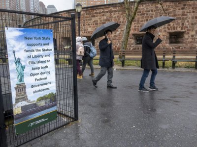 Des passants devant une pancarte expliquant que New York paie pour garder la Statue de la Liberté ouverte aux touristes, alors que les Etats-Unis entrent dans leur troisième semaine de "Shutdown", le 5 janvier 2019 à New York - DON EMMERT [AFP]