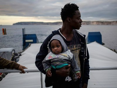Un migrant tenant un bébé regarde la côte maltaise depuis le pont du Sea Watch 3, le 9 janvier 2019 - FEDERICO SCOPPA [AFP]