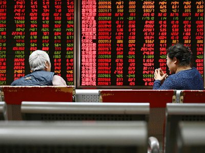 Deux femmes assises devant un écran montrant l'évolution des cours boursiers, le 21 janvier 2019 à Pékin - GREG BAKER [AFP]