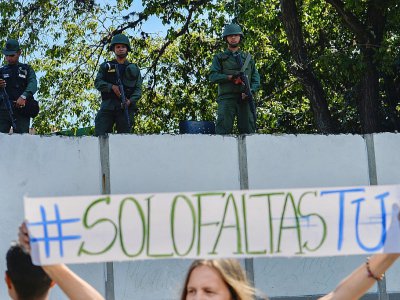 Une femme brandit une pancarte "#Il ne manque que toi" devant des soldats surveillant un quartier général de l'armée, à Caracas le 27 janvier 2019 - Luis ROBAYO [AFP]