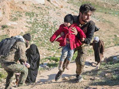 Un combattant des Forces démocratiques syriennes (FDS), soutenues par Washington, aide une femme et ses enfants ayant fui l'ultime poche du groupe jihadiste Etat islamique (EI), le 13 février 2019 - Fadel SENNA [AFP]
