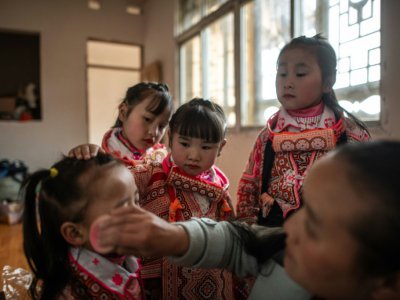 Une femme maquille des jeunes filles de l'ethnie des "Miao à longues cornes" pour la Fête des fleurs, le 14 février 2019 à Longjia, en Chine - FRED DUFOUR [AFP]