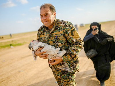 Un membre de la force antijihadiste arbo-kurde porte un bébé suivie par une femme qui vient de quitter le dernier réduit du groupe Etat islamique (EI) près de Baghouz, dans l'est de la Syrie, le 22 février 2019 - Bulent KILIC [AFP]