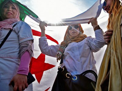 Des Algériennes sous un grand drapeau du pays lors de la manifestation d'enseignants et d'élèves contre l'extension du quatrième mandat d'Abdelaziz Bouteflika, le 13 mars 2019 à Alger - RYAD KRAMDI [AFP]