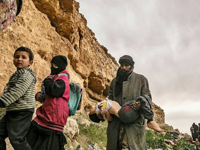 Un homme avance en tenant dans ses bras tendus devant lui un enfant immobile après être sorti du dernier réduit du groupe Etat islamique en Syrie, le 14 mars 2019 - Delil souleiman [AFP]