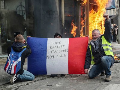 Des "gilets jaunes" brandissent un drapeau français sur lequel est écrit "liberté, égalité, fraternité, mon cul!" alors qu'un kiosque à journaux flamble sur les Champs-Elysées à Paris le 16 mars 2019 - Zakaria ABDELKAFI [AFP/Archives]