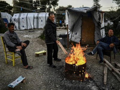 Des hommes se réchauffent autour d'un feu de bois dans le camp de réfugiés de Moria sur l'île grecque de Lesbos, le 19 mars 2019 - ARIS MESSINIS [AFP]