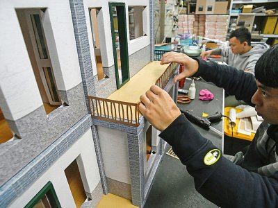 Un employé d'une société spécialisée dans la fabrication d'offrandes en papier fixe le balcon d'une maison, le 7 mars 2019 à Taïwan - SAM YEH [AFP]
