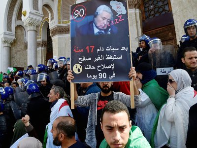 Lors d'une manifestation le 10 avril 2019 à Alger, un manifestant brandit une pancarte où figure Abdelkader Bensalah et est écrit en arabe: "Après 17 ans de coma, le malade s'est réveillé pour régler notre situation en 90 jours" - RYAD KRAMDI [AFP]