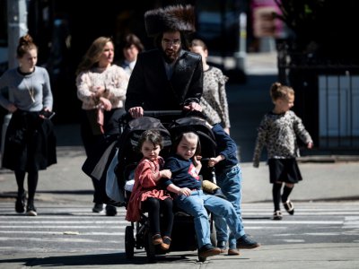 Un homme traverse une rue avec ses enfants, dans le quartier de Williamsburg Brooklyn à New York, qui compte une importante population juive orthodoxe, le 24 avril 2019 - Johannes EISELE [AFP]