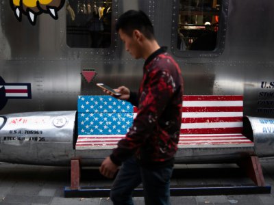 Un homme passe devant un banc décoré d'un drapeau américain devant un magasin à Pékin le 15 mai 2019 - FRED DUFOUR [AFP/Archives]