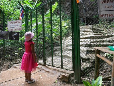 Une fillette devant l'entrée de la grotte de Tham Luang où des adolescents de l'équipe de foot des "Sangliers sauvages" sont restés bloqués en 2018, le 13 juin 20189 à Mae Sai, en Thaïlande - Lillian SUWANRUMPHA [AFP]