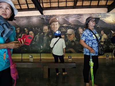Des touristes photographient une fresque relatant le sauvetage des adolescents thaïlandais en 2018 à l'entrée de la grotte de Tham Luang, le 13 juin 2019 à Mae Sai - Lillian SUWANRUMPHA [AFP]