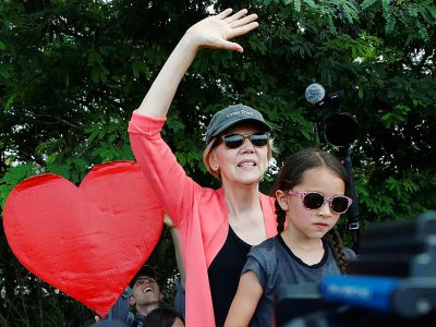 Elizabeth Warren, accompagnée d'une fillette, fait un geste en direction de migrants mineurs logés dans un centre de rétention à Homestead, en Floride, le 26 juin 2019 - RHONA WISE [AFP]