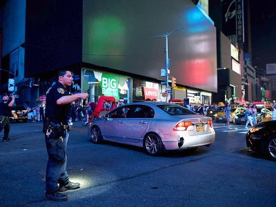 Un policier assure la circulation devant les panneaux publicitaires lumineux de Times Square éteints suite à une panne d'électricité géante, le 13 juillet 2019 à New York - Johannes EISELE [AFP]
