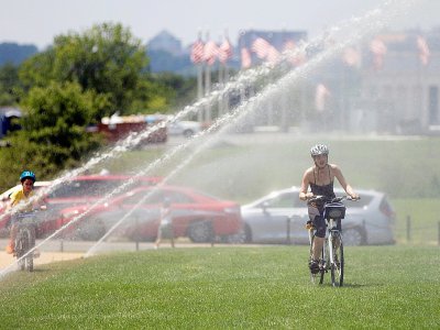 Des cyclistes roulent sous les jets d'une fontaine à Washington le 19 juillet 2019 - Alastair Pike [AFP]