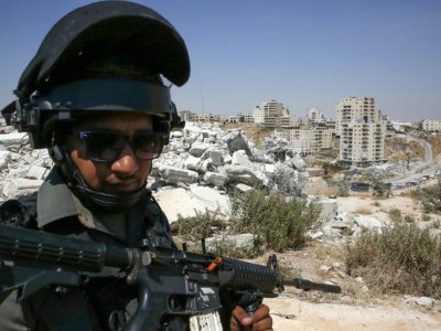 Un policier aux frontières israélien monte la garde devant des bâtiments démolis par Israël dans le quartier palestinien de Sour Baher, le 22 juillet 2019 - HAZEM BADER [AFP]