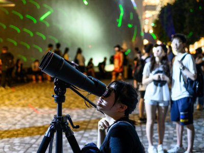 Une manifestante regarde dans un télescope pendant une manifestation en forme de spectacle laser, le 7 août 2019 à Hong Kong - Philip FONG [AFP]