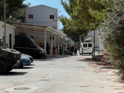 Des policiers et des migrants devant l'entrée du centre d'accueil de Lampedusa, le 21 août 2019, en Sicile - Taimaz SZIRNIKS [AFP]