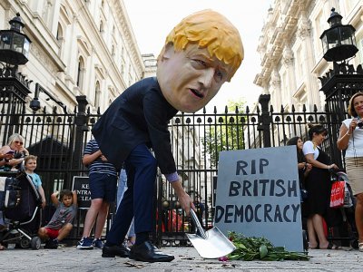 Un manifestant portant un masque représentant le Premier ministre britannique Boris Johnson manifeste devant les bureaux de ce dernier à Downing Street en installant une fausse pierre tombale, le 28 août 2019 à Londres. - DANIEL LEAL-OLIVAS [AFP]