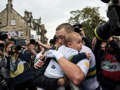 L'Australien Rohan Dennis, champion du monde du contre-la-montre, prend son épouse et son enfant dans les bras à l'arrivée, le 25 septembre 2019 à Harrogate (Angleterre) - OLI SCARFF [AFP]