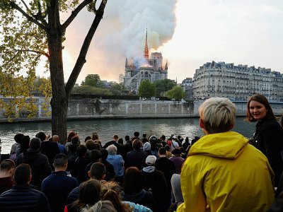 Des passants regardent les flammes dévorer la toiture de la cathédrale Notre-Dame, le 15 avril 2019 à Paris - GEOFFROY VAN DER HASSELT [AFP/Archives]