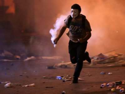 Un manifestant masqué court avec une grenade lacrymogène lors de heurts avec les forces de sécurité, le 18 octobre 2019 à Beyrouth, au Liban - - [AFP]