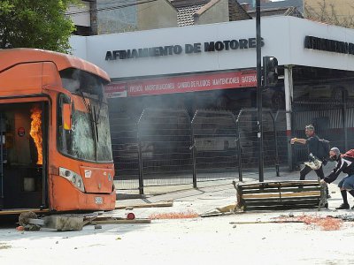 Des manifestants montent une barricade près d'un bus en flammes durant des émeutes à Santiago, le 19 octobre 2019 - Martin BERNETTI [AFP]