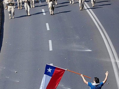 Un protestataire tenant un drapeau chilien s'avance vers des soldats durant des manifestations à Santiago, le 20 octobre 2019 - CLAUDIO REYES [AFP]
