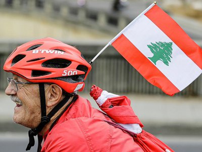 Un cycliste libanais chevauche avec un drapeau national à travers la région de Dbayeh au nord de Beyrouth, en soutien aux protestations au Liban contre l'élite dirigeante et les conditions économiques désastreuses, le 23 octobre 2019 - JOSEPH EID [AFP]