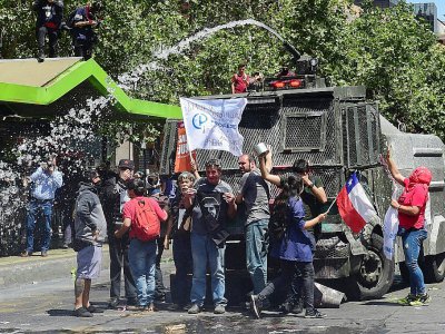 Des manifestants se tiennent devant un canon à eau de la police, à Santiago le 23 octobre 2019 - Martin BERNETTI [AFP]