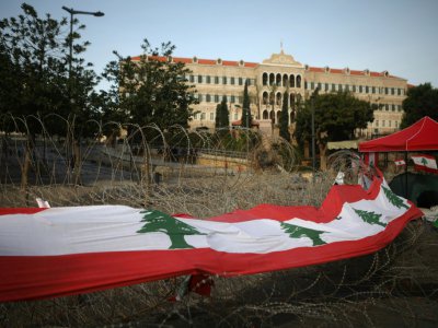 Un large drapeau libanais placé sur les barbelés devant le siège du gouvernement à Beyrouth, le 26 octobre 2019 - Patrick BAZ [AFP]