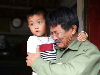 Le Minh Tuan, qui craint que son fils soit parmi les morts trouvés dans un camion en Grande-Bretagne, avec son petit-fils, devant leur maison dans le centre du Vietnam, le 27 octobre 2019 - NHAC NGUYEN [AFP]