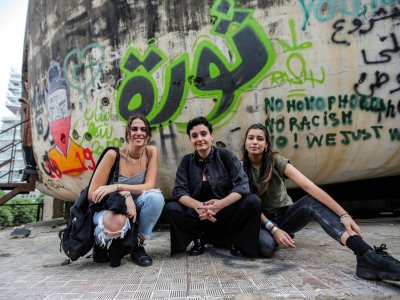 De jeunes Libanaises posant devant "L'oeuf", une structure emblématique en béton au toit oblong à moitié en ruines, recouvert de graffittis dont le mot "Revolution" en vert en arabe, à Beyrouth le 24 octobre 2019 - ANWAR AMRO [AFP]