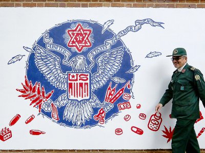 Un Gardien de la Révolution iranien passe devant une fresque murale sur l'enceinte de l'ancienne ambassade américaine à Téhéran, le 2 novembre 2019 - ATTA KENARE [AFP]