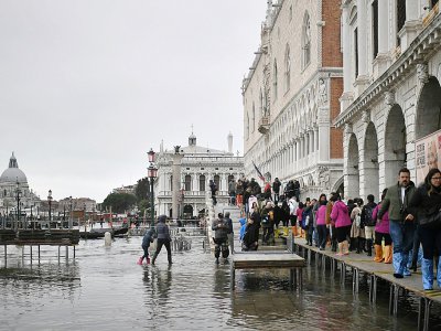 Des piétons marchent sur une passerelle au dessus d'un quai inondé, à Venise le 13 novembre 2019 - Marco Bertorello [AFP]