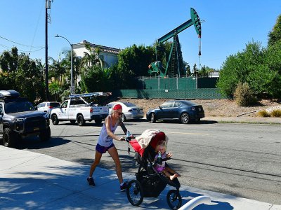 Une femme et sa fille de 2 ans dans une poussette devant une pompe à pétrole le 21 octobre 2019 à Signal Hill, en Californie - Frederic J. BROWN [AFP]