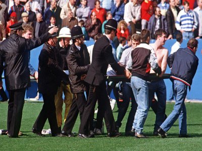 Des policiers et des supporters aident à évacuer des blessés du stade d'Hillsborough (Royaume-Uni) le 15 avril 1989, où une bousculade a coûté la vie à 96 personnes - STRINGER [AFP/Archives]