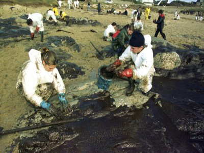 Des bénévoles nettoient à la main les rochers d'une crique de la côte sauvage du Croisic, le 29 décembre 1999, suite au naufrage du pétrolier maltais Erika le 12 décembre dernier - FRANK PERRY [AFP/Archives]