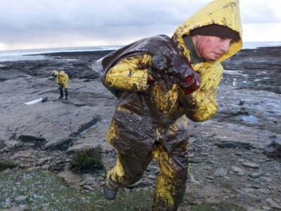 Un militaire porte un sac rempli de pétrole, le 28 décembre 1999 sur une plage de la pointe des chats, sur l'Ile de Groix, dans le Morbihan - EMMANUEL PAIN [AFP/Archives]