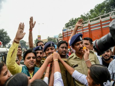 Des écoliers offrent des friandises à des policiers à Ahmedabad le 6 décembre 2019, lors d'un rassemblement populaire pour se réjouir de la mort de quatre suspects d'un viol qui a choqué l'Inde - SAM PANTHAKY [AFP]
