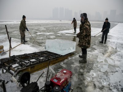 Des travailleurs utilisent un tapis roulant pour transporter des blocs de glace découpés dans la rivière Songhua, le 12 décembre 2019 à Harbin, en Chine - NOEL CELIS [AFP]