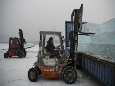 Des travailleurs chargent sur des camions des blocs de glace découpés dans la rivière Songhua, le 10 décembre 2019 à Harbin, en Chine - NOEL CELIS [AFP]