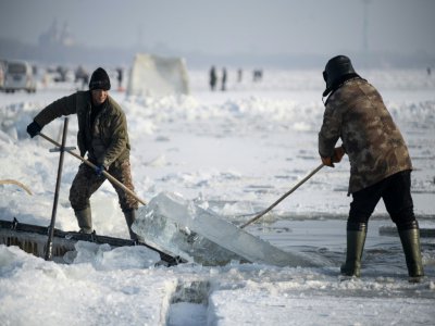 Des travailleurs sortent un bloc de glace de la rivière Songhua, le 12 décembre 2019 à Harbin, en Chine - NOEL CELIS [AFP]