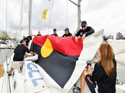 L'équipage du "Tribal Warrior" (Guerrier Tribal) hisse le drapeau aborigène dans le port de Sydney en Australie, le 13 décembre 2019, lors d'un exercice avant le départ de la course Sydney-Hobart ce jeudi. - Saeed KHAN [AFP]