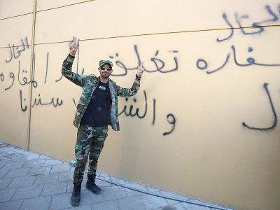 Un membre du Hachd al-Chaabi, coalition de paramilitaires dominée par des factions pro-Iran, fait le V de la victoire devant un graffitti en arabe sur le mur de l'ambassade des Etats-Unis à Bagdad, qui affirme : "l'ambassade américaine est fermée sur - AHMAD AL-RUBAYE [AFP]