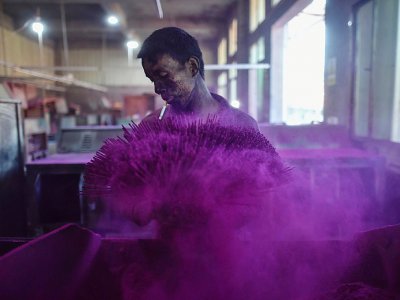 Un travailleur couvre des bâtonnets d'encens avec de la poudre colorée dans une fabrique à Quanzhou, en Chine - HECTOR RETAMAL [AFP]