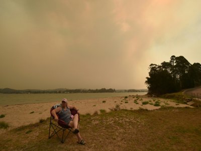 Une femme observe depuis la plage où elle s'est réfugiée un incendie qui fait rage, à Batemans Bay en Australie le 4 janvier 2020 - PETER PARKS [AFP]