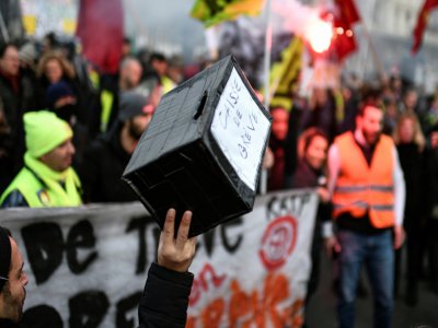 Un homme tient une caisse pour soutenir les grévistes, dans une manifestation à Paris le 26 décembre 2019 - STEPHANE DE SAKUTIN [AFP/Archives]