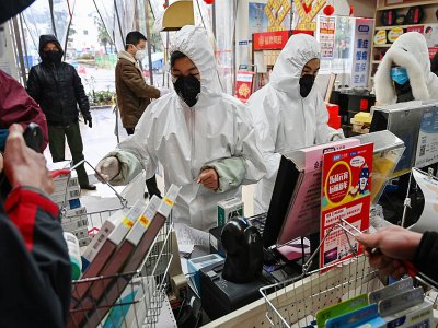 Des employés en pharmacie, en combinaison et masque de protection, servent des clients, le 25 janvier 2020 à Wuhan, épicentre du nouveau coronavirus - Hector RETAMAL [AFP]